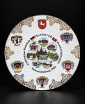 PORCELANA, um (1) prato comemorativo em porcelana na tonalidade branca alusivo à EXPO 2000  Hannover World Exposition / Weltausstellung 2000, Alemanha, com decoração policromada representando pontos turísticos de Hannover, bandeiras e brasões de Niedersachsen, Berlin, Celle, Hamburg, Hannover e Bundesrepublik Deutschland, além de ornamentos dourados na borda, medindo 26cm de diâmetro, leves falhas na pintura.