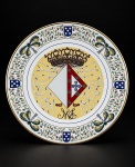 PORCELANA, um (1) prato comemorativo em porcelana na tonalidade branca, edição limitada, criado por José Bernard Guedes  Colecções Philae, em homenagem a Sua Alteza Real a Infanta D. Maria Francisca Isabel Micaela Gabriela Rafaela Paula de Herédia e Bragança, por ocasião de seu batizado em Vila Viçosa, na Igreja de Nossa Senhora da Conceição, em 31 de maio de 1997. Apresenta decoração heráldica policromada com coroa, brasões e laços, com filete dourado na borda, medindo 24cm de diâmetro.