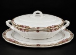 Sociedade de Porcelana de Coimbra (S.P. Coimbra), uma (1) sopeira com presentoir confeccionadas em porcelana portuguesa na tonalidade branca, ricamente decorada por guirlanda floral, vegetalista e geométrica em policromia com filetes na cor verde, sopeira medindo 12x33x17,5cm e presentoir, medindo 34,5x23cm.