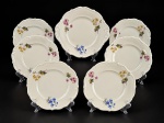 Carl Tielsch & Co., conjunto para bolo com sete (7) peças confeccionadas em porcelana alemã na tonalidade creme, decorada por elementos florais e vegetalistas em policromia, realces em relevo na pasta e borda com filete verde, sendo: A) 1 prato para bolo, medindo 27x24,5cm e B) 6 pratos para sobremesa, medindo 20cm. Prato para bolo com imperceptível bicado na borda.