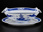 PORCELANA CHINESA, uma (1) molheira fixada ao presentoir confeccionada em porcelana oriental na tonalidade branca, decorada por cena com pagodes, elementos florais e vegetaistas, espessas faixas geométricas na técnica BLUE and WHITE, medindo 8,5x22,5x14cm.