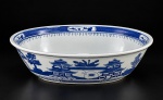 PORCELANA CHINESA, uma (1) travessa oval e funda confeccionada em porcelana oriental na tonalidade branca, decorada por cena com pagode, elementos florais e vegetaistas, espessas faixas geométricas na técnica BLUE and WHITE, medindo 7x25,5x18,5cm.
