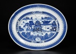 PORCELANA CHINESA, uma (1) travessa oval confeccionada em porcelana oriental na tonalidade branca, decorada por cena com pagodes, elementos florais e vegetaistas, espessas faixas geométricas na técnica BLUE and WHITE, medindo 30,5x22,5cm.