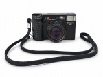 FOTOGRAFIA, uma (1) câmera fotográfica analógica vintage, marca CANON, modelo ML, com sistema de foco automático (Auto Focus), lente Canon, flash embutido e visor óptico. Corpo em material sintético preto, com detalhes texturizados e alça de transporte. Apresenta sinais de uso e marcas do tempo. Funcionamento não testado. No estado.