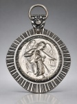 ARTE SACRA, uma (1) medalha de berço confeccionada em metal espessurado a prata, com cena em relevo representando Anjo da Guarda acompanhando uma criança, cercada por moldura ornamentada com friso radial. Parte superior decorada com motivo floral em relevo e argola para suspensão, medindo 8x6,5cm.