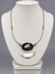 BIJUTERIA, um (1) colar confeccionado em metal prateado, de design modernista, composto por corrente de elos, segmentos tubulares e pingente central com cabochão oval em material distinto de tonalidades roxa, creme e escura, montado sobre elemento metálico vazado e articulado, medindo aberto 44cm de comprimento aberto.