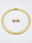 BIJUTERIAS, duas (2) peças confeccionadas em metal dourado, sendo: A) 1 gargantilha rígida e articulável, formado por elos largo e fecho tipo encaixe, medindo 40cm de comprimento aberto e B) par de brincos em formato de laço, cravejados com pedras incolores, medindo 1,5x1,5cm.