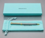 CANETA, uma (1) caneta esferográfica da manufatura Tiffany & Co., confeccionada em metal prateado com detalhes dourados, incluindo clip estilizado e acabamento bicolor. Acompanha estojo original Tiffany & Co. na tradicional tonalidade azul-turquesa e saquinho protetor da marca. Apresenta desgastes na caixa e inscrições a caneta, necessita de nova carga.