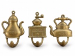 METAL DOURADO, três (3) ganchos decorativos de parede, em metal dourado, representando cafeteira, moedor de café e chaleira, com detalhes florais em relevo e ganchos inferiores, medindo 8,5x5cm e menor 7,5x6cm.