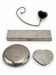 METAL PRATEADO, quatro (4) acessórios de toucador, em metal prateado, sendo: A) um (1) gancho porta-bolsa, com aplicação em formato de coração preto, medindo 10,5cm de comprimento, B) um (1) estojo retangular de maquiagem LANCÔME, com gravação decorativa, apresentando sinais de uso, ausência dos pincéis, medindo 15,5x4,5cm e C) um (1) trousse ricamente gravado com arabescos, medindo 8,5cm e D) um (1) estojo em formato de coração, medindo 5,5x6cm. Apresentam sinais de uso e pátina. Peças no estado.