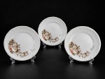 PORCELANA SCHMIDT, três (3) pratos rasos confeccionados em porcelana nacional na tonalidade branca, decorada por flores e folhagens em policromia, elementos em relevo na pasta e borda filetada em prata, medindo 25,5cm.