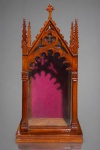 ARTE SACRA, um (1) oratório em madeira entalhada, ao estilo neogótico, com estrutura arquitetônica em forma de capela, cobertura em duas águas, arcos ogivais, ornamentos vazados em motivos trilobados, pináculos trabalhados e remate superior em cruz estilizada. Apresenta porta frontal e laterais envidraçadas, interior com fundo revestido em tecido vermelho-vinho e base escalonada, medindo 84,5x41x28cm.