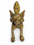 BRONZE, uma (1) aldrava confeccionada em bronze, composição zoomórfica, representando cabeça e patas de canídeo, possivelmente lobo, com elementos em relevo e furação superior para fixação, medindo 16,5cm.