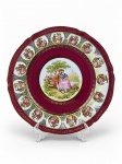 PORCELANA DE BAVARIA, um (1) medalhão confeccionado em porcelana alemã na tonalidade branca, ricamente decorada por cenas galantes de diferentes modelos em policromia, guirlandas florais em vasta douração sobre fundo vinho, borda filetada a ouro com falhas na douração, medindo 32,5cm.