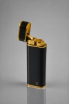 COLECIONISMO, um (1) isqueiro de bolso CARTIER PARIS, de formato retangular alongado com extremidades arredondadas, confeccionado em metal dourado e corpo revestido em laca preta, apresentando detalhes e frisos dourados. Tampa superior articulada, com mecanismo de acendimento por roldana e pederneira. Ostenta o tradicional monograma duplo C da Cartier na parte frontal e inscrições Cartier Paris, além de numeração de série gravada na base. Peça de requintado desenho, ao estilo dos acessórios de luxo franceses. Apresenta marcas de uso, pequena mossa, necessita revisão, medindo 7x2,5x1,5cm.