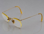 ÓCULOS, um (1) óculos de grau, estilo vintage, apresentando armação delicada em metal dourado, com marcação 1/10 12K GF, indicativa de acabamento em ouro laminado de 12 quilates (Gold Filled). Lentes transparentes de formato ovalado, ponte nasal arqueada, plaquetas de apoio em material de tonalidade âmbar e hastes metálicas finas, ornamentadas com delicados trabalhos geométricos gravados, terminadas em ponteiras curvas de tonalidade amarelada. Apresenta sinais de uso, acondicionado em estojo com oxidações, medindo 4x13x16cm.