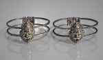 BIJUTERIAS, par (2) de braceletes confeccionados em metal prateado, 2 elos circulares em vazado com cabeça de leão em relevo, sinais de uso, medindo 6,5cm de diâmetro.