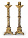 ARTE SACRA, um (1) par de castiçais de altar para uma vela em bronze, com hastes torneadas, fustes ornamentados em espiral, bobeches com decoração floral em relevo e bases trípodes com medalhões representando figuras sacras. Um dos castiçais apresenta repintura posterior, com diferenças na tonalidade e no acabamento em relação ao outro. Medida :  50cm , um dos bocais solto .