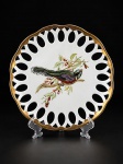 SCHMIDT  SANTA CATARINA, um (1) prato decorativo em porcelana branca vitrificada, com bordas vazadas, realçadas em dourado, apresentando pintura à mão de ave sobre galho , intitulada "Trogon Ambiguus". Peça assinada e marcada no verso . Medida : 27 cm