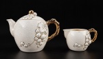 FAIANÇA JAPONESA, um (1) conjunto composto por 2 peças, sendo um bule para chá  com tampa e uma leiteira, em faiança esmaltada craquelada, com decoração em relevo de cachos de uvas e folhagens, realces dourados e alças ornamentadas imitando galhos. Leiteira apresenta bicado na borda.