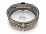 METAL PRATEADO, uma (1) caixa porta joias confeccionada em metal espessurado a prata, cinzelada por faixa floral em relevo e perolado, recipiente interno e tampa em cristal com lapidação estrelada no fundo, apresenta falhas no banho, medindo 7x18,5cm.