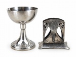WMF (Württembergische Metallwarenfabrik), duas (2) peças, sendo: A) 1 calice art noveau, corpo bojudo, base cônica com cinzel geométrico, medindo 12x9xcm e B) 1 porta guardanapo com cinzelado art noveau, em estanho com desgastes e mossa na peça, medindo 8,5x9cm.