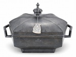 ESTANHO, uma (1) sopeira sextavada confeccionada em estanho, tampa em caneluras, pega torneada em bilro, alças laterais vazadas, etiqueta na peça, apresenta marcas do tempo, medindo 25,5x38x22,5cm.