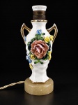 ABAJUR - Um (1) abajur para uma lâmpada confeccionado em porcelana branca, com corpo em formato de ânfora, duas alças laterais com detalhes dourados e rica decoração floral policromada em alto-relevo, com aplicação de rosas e flores. Base circular em pedra, instalação elétrica no estado . Medida : 23 cm , apresenta falhas na douração .