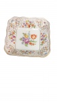 Prato Quadrado em Porcelana Alemã Schumann Bavaria (c. 1945-1949). Formato quadrado com abas onduladas e relevos em volutas floreadas realçados a douração. Decoração policromada com buquê floral ao centro e detalhes nas bordas. No verso, marcação de manufatura "Schumann Bavaria Germany US Zone" (período de ocupação americana pós-Segunda Guerra Mundial, 1945-1949)  medindo  3 x 14 cm  diâmetro