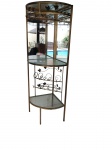 BAR DE CANTO / CRISTALEIRA Estrutura em ferro trabalhado com pátina dourada e detalhes decorativos aplicados em formato de folhagens. Fundo espelhado, prateleiras em vidro incolor e suporte superior integrado para pendurar taças, além de nichos dedicados para garrafas na seção inferior. Medidas: 1,80 x 0,50 x 0,50 Marcas do tempo de uso .Retirada com agendamento na Barra da Tijuca