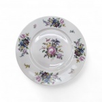 Art Déco (circa 1925-1941). Prato em porcelana de pasta dura alemã, fabricado por C. Teichert (Meissen) em Selb, Baviera (marca "V"), para a marca da importadora Black Knight (Graham & Zenger, NY). Decoração policromada em estilo Deutsche Blumen, apresentando buquê central assimétrico com "Rosa de Meissen", amores-perfeitos e tulipas, além de buquês secundários e ramos dispersos na aba. Pintura botânica detalhada. Diâmetro: 25 cm. Bom estado de conservação,   no verso e suporte para parede adaptado .Diâmetro 25 cm