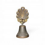 Sineta de chamada manual articulada em bronze com pátina escura do tempo. O espelho de fixação apresenta formato estilizado de concha vieira com orifício para instalação. O sino possui duas linhas incisas decorativas na saia. Meados do Século XX. Bom estado de conservação, com marcas de desgaste naturais que evidenciam a antiguidade da peça. medida total 15 cm de altura.