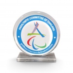 Placa / Troféu Comemorativo do Comitê Paralímpico da Tailândia  em formato circular sobre base retangular, confeccionada em acrílico transparente. Apresenta ao centro a insígnia oficial do Paralympic Committee of Thailand o símbolo dos três Agitos  .Dimensões: Placa: 18 x 18 cm | Base: 1 x 6 x 17 cm. Excelente estado.