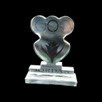Troféu em Acrílico - Comitê Olímpico da Jordânia Placa  comemorativa em acrílico transparente maciço, com os Anéis Olímpicos e o símbolo do Comitê Olímpico Jordaniano. Base retangular gravada "JORDAN". Apresenta leves marcas de manuseio e tempo. Vendido no estado.    medindo 17 x 10 cm e  da Base: 2 x 4,5 x 15 cm