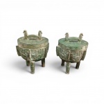 Par de Vasos Rituais Tripodes em ferr fundido  Estilo Arcaico Chinês  com tampa (estilo Ding), confeccionados em bronze fundido com pátina esverdeada induzida que simula oxidação arqueológica. O corpo e os pés cilíndricos apresentam ornamentação em relevo com o clássico padrão zoomórfico Taotie. As tampas possuem alças estilizadas em formato de aves. Base marcada em relevo circular "MADE IN TAIWAN", meados do século XX,  Dimensões: 32 x 23 cm (cada).    desgaste  marcas de fundição e pátina da manufatura do período.