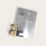 PORTA-RETRATO COM ESCULTURA DE PIETRINA CHECCACCI em acrílico transparente (17 x 12 cm), ornamentado com escultura em bronze de torso feminino (7 cm), bom estado .  Peça sem assinatura.