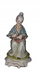 CAPODIMONTE (ITÁLIA)  "A Costureira"Escultura em porcelana italiana policromada representando senhora em afazeres manuais. Marcada na base N coroada, Capodimonte Made in Italy). Altura: 23 cm.