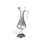 Jarro oriental em metal trabalhado. Corpo piriforme cinzelado com motivos florais e geométricos, gargalo alongado e alça sinuosa (estilo aftaba). Apresenta pátina e desgastes naturais do tempo.Medidas: 20 cm de altura.