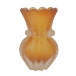 Vaso floreiro  em vidro artístico de Murano fosco na cor âmbar. Ele apresenta um design clássico com corpo arredondado em gomos (canelado), gola cinturada com pequenas alças decorativas nas laterais e uma elegante borda ondulada em formato de babado. Arte decorativa e de design moderno.