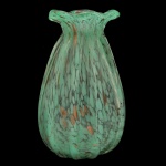 Vaso em vidro artístico de Murano com seu acabamento verde jade com efeito mesclado, que traz salpicos e inclusões douradas (pó de aventurina), conferindo uma textura visual orgânica e sofisticada. Apresenta um formato de gota com canelados verticais bem-marcados e uma borda ondulada na boca, simulando gomos. Arte decorativa e de design moderno.