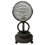 Original luminária montada com estrutura metálica centralizando placa circular em cristal acetinado, moldada com figura de Medusa com 2 rostos. Montagem de cor preta, com iluminação por trás da figura, apoiada em anelado sobre base circular com 2 degraus superpostos e pés de bolota. Fiação nova. 33 x 15 x 18 cm.