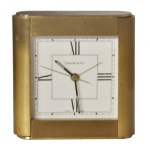 TIFFANY & Co. Relógio de mesa em latão maciço, com mostrador branco, algarismos romanos pretos e movimento quartz suíço. A peça traz uma gravação personalizada no topo em homenagem a um casal ("Mom and Leonard") com a data de 17 de novembro de 1990. O mostrador clássico apresenta numerais romanos nas posições principais, ponteiros pretos e a assinatura da famosa joalheria nova-iorquina ao centro.10 x 6 cm. Necessita passar por um relojoeiro para alguns ajustes.