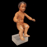 Circa de 1800 - Imagem em madeira clara do Menino Jesus. Apresenta-se desnudo, em posição sentada, com os braços à frente. Notam-se o delicados cachos do cabelo e a intensa expressão do olhar. Defeitos e perdas na mãos. Base em acrílico. 43 x 25 x 17 cm. 50 x 25 x 20 cm (MT).