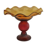 Fruteira de pé alto vidro com pé, estilo amberina,  caracterizado pela cor que gradua do vermelho para o amarelo âmbar. Apresenta borda ondulada e haste balaústre  26 x 30 cm.