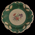 SCHWARZENHAMMER, Alemanha - Prato em porcelana alemã.  Apresenta uma borda ondulada verde com detalhes dourados e flores policromadas. Centro decorada com um ramalhete de flores e detalhes vazados na borda. Marca da manufatura no verso. 32 cm.