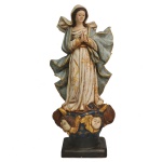 Imagem de N. Sra. da Conceição em estuque (revestimento feito à base de gesso, areia e pó de mármore), policromada e dourada. Apresenta-se em sua tradicional postura com as mãos em oração e o olhar virado para baixo. Exibe ricas vestes, amplamente pregueadas, compostas por um véu sobre os cabelos, uma túnica com longos plissados, bordada a ouro com motivos florais, e um esvoaçante manto azul celeste realçado por adornos dourados. Base formada por globo com estrelas, cabeças de anjos e lua. Peanha retangular. Olhos de vidro. 45 x 20 x 12 cm.