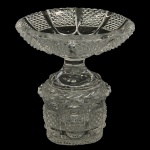 BACCARAT - Centro de mesa com pedestal, em espesso cristal translucido e lapidado com ricos detalhes geométricos. Apresenta bacia superior aberta com borda trabalhada, encaixada sobre uma base pedestal robusta e ornamentada em alto relevo e lapidação artesanal detalhada. 14 x 14 cm.