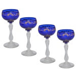Conjunto de 4 delicados taças de pé alto em cristal da Boêmia, com bojos de cor azul, de formato ballon achatado, ornados por volutas em guirlandas ondulantes e douradas. Hastes retas e abauladas, realçadas por anelados nas extremidades, apoiadas em pés circulares.16 cm.