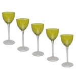 Conjunto de 5 taças em cristal da Boêmia, com bojos cônicos de cor verde lima, lapidados e ornamentados por raiados distribuídos em reservas triangulares. Hastes retas e facetadas, apoiadas em pés moldados com gomos em leque.18 cm.