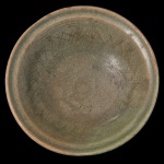 CHINA. Ming (1368-1644) - Prato circular em porcelana chinesa, revestido por coberta celadon de cor esverdeada com discreto craquelê. Apresenta decoração incisa com adornos em cruz centralizando anelado liso, e finos filetes. Borda moldada em debrum. Fornos de Longquan.  Ming (1368-1644).  Bicado na base. 5 x 16 cm.